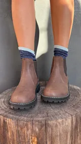 Botas Chelsea de cuero color marrón, con elástico lateral, suela negra gruesa y pespuntes blancos.