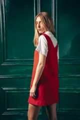 Vestido corto color rojo, con escote en V, sin mangas y dos bolsillos frontales. Se usa sobre una camisa blanca de mangas cortas con cuello clásico.