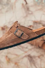 Zueco marrón de gamuza con hebilla metálica ajustable.