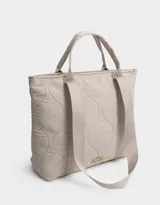 Bolso tipo shopper color beige, con diseño acolchado y pespuntes ondulados. Tiene doble asa de hombro y correa extraíble regulable.