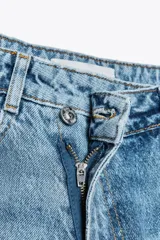 Jeans tobilleros de tiro alto color blanco, corte recto y bajo sin costura. Cierre frontal cruzado con cremallera y botones.