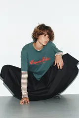 Camiseta de manga corta color verde azulado (teal) con efecto lavado, corte oversize y cuello redondo. Estampado frontal en color rojo con el texto "Sapore Felice" en tipografía cursiva.