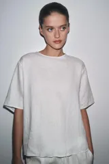 Top de lino color blanco, con cuello redondo y mangas cortas. Detalle de abertura en la espalda ajustable con lazadas.
