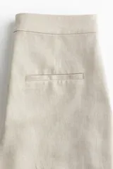 Pantalón de vestir color beige claro, de corte amplio y largo cropped. Confeccionado en tejido de mezcla de lino y viscosa, de tiro alto con cierre, botón oculto y corchete.