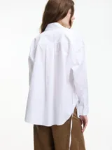 Camisa blanca de algodón con cuello camisero y cierre frontal con botones.