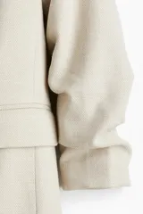 Blazer color crema con solapas de muesca, mangas tres cuartos fruncidas y bolsillos delanteros con solapa. Sin cierre. Forrado.