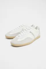 Zapatillas deportivas blancas con detalles plateados y suela color caramelo.