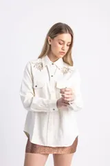 Camisa color crema en gabardina de algodón orgánico, estilo cazadora, con cinto en la cintura y aplique bordado a mano en hilo de lino en la parte superior.