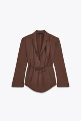 Blazer marrón con cuello solapa, manga larga con hombreras y cierre frontal con botones. Incluye cinturón fino del mismo tejido para ajustar a la cintura.