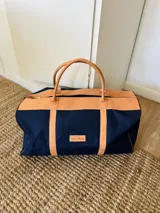 Bolso de lona azul marino con detalles en cuero color suela. Tiene doble asa de mano y cierre superior con cremallera.
