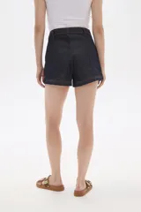 Short de jean oscuro, tiro alto, con pespuntes en color naranja y diseño de paneles frontales que simulan bolsillos curvos. Cierre frontal con botón dorado.