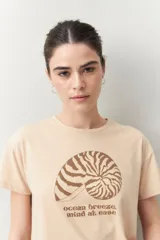 Remera blanca de manga corta con estampado de una concha marina y la frase "ocean breeze, mind at ease" en color marrón.