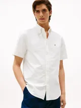 Camisa blanca de corte regular, confeccionada en algodón Oxford con cuello abotonado, manga corta y logo de Tommy Hilfiger bordado en el pecho.