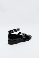 Zapato tipo zueco negro charol con punta fina, doble tira con hebillas metálicas y pulsera al tobillo con tachas.