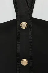 Top negro de tejido elástico con cuello halter y espalda descubierta. Presenta falsos bolsillos con botones metálicos en el delantero y cierre frontal con botones metálicos.