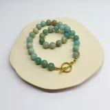 Collar de cuentas de amazonita de 10 mm de diámetro, con separadores de hilo color turquesa y cierre de mosquetón de acero hipoalergénico con baño dorado.