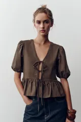 Top amarillo de escote pico y manga corta abullonada con elástico. Detalle de combinación de tejidos a tono y bajo con volante. Cierre frontal con lazadas.