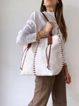 Bolso tipo tote bag de cuero color crudo con detalles de costuras y tiras de cuero marrón.