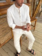 Camisa blanca de corte clásico con cuello mao, manga larga con puños abotonados y cierre frontal con botones de madera.