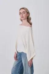 Sweater holgado de tejido ligero, color beige claro, con escote asimétrico que deja un hombro al descubierto.