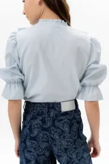 Blusa de lino color rojo con volados frontales que enmarcan el pecho, cuello redondo con mini volado y mangas 3/4 abullonadas con puño elástico. Presenta un cierre frontal con botones y una silueta relajada.