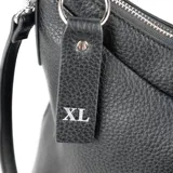 Cartera tipo gondola color negro, confeccionada en cuero sintético graneado. Tiene acceso con cierre, un compartimento principal con un bolsillo interno con cierre y otro abierto. Incluye correa regulable y asa fija. Los herrajes son plateados.