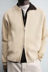 Chaqueta de punto color mostaza, corte relaxed fit, con cuello elástico, manga larga, bolsillos en la cadera, acabados en rib y cierre frontal con cremallera.
