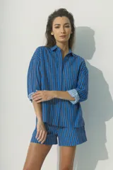 Camisa celeste a rayas verticales azules y negras, de corte holgado, manga 3/4 con puños doblados y cuello clásico.