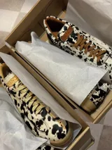 Zapatillas bajas con estampado animal print de vaca en blanco y negro, con cordones marrones y suela color caramelo.