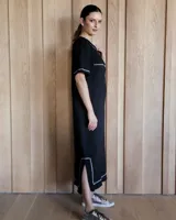 Vestido midi negro con cuello redondo y mangas cortas. Presenta dos bolsillos cuadrados en el pecho y ribetes blancos en cuello, mangas, bolsillos y ruedo.