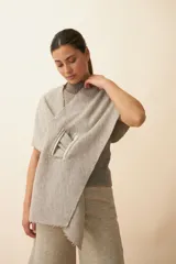 Chal asimétrico de lana color gris claro, con cortes en los hombros y doble ojal de fieltro para mantener el cruce. Terminación pespunteada y al corte.