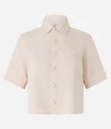 Camisa color beige claro, corta, con cuello inglés, manga corta, bolsillo en el pecho y abotonada adelante.