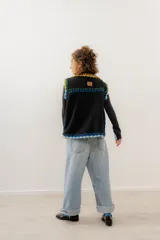 Chaleco negro de corderito con cierre de alamares y tejido a mano en crochet con detalles en amarillo, verde, celeste y azul.