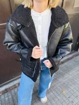 Campera negra estilo aviador, con cuello y forro de piel sintética. Cierre frontal con cremallera y hebilla en el cuello. Bolsillos laterales con solapa y puños ajustables con hebilla.