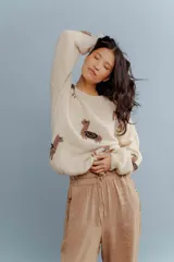 Sweater color crema tejido en lana merino con cuello redondo y mangas largas. Presenta diseño de llamas marrones con detalles en zigzag negros.