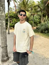 Remera beige de algodón con estampa en la espalda de una flor sonriente sobre un fondo a cuadros azules y texto "FLOWKERS".