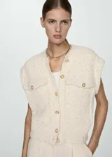 Chaleco de tweed color crema con lentejuelas, cuello redondo, cierre frontal con botones dorados y dos bolsillos de parche con botón.