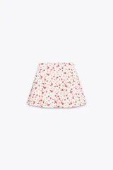 Falda mini con estampado de cerezas rojas sobre fondo blanco, de corte evasé con tablas y cierre lateral oculto.