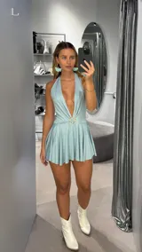 Minivestido celeste con escote halter pronunciado y espalda descubierta. Presenta un aplique circular con strass en la cintura y falda con volados.