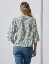Blusa de gasa estampada con flores verdes sobre fondo blanco, de la marca Sioni. Tiene mangas cortas amplias con abertura y botón.