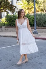 Vestido midi blanco de corte princesa, con breteles finos, escote en V, botones frontales, plisados en el torso y bordados de encaje en cintura y ruedo.