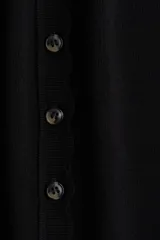 Saco corto negro de punto fino suave con cuello redondo, mangas cortas y botonadura frontal. Tiene ribete festoneado en tapeta, mangas y bajo.