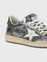 Zapatillas Golden Goose modelo Ballstar, caña baja, con capellada y lengüeta de glitter negro/plateado. Presentan puntera laminada oscura y estrella lateral blanca. La suela es de goma con efecto desgastado.
