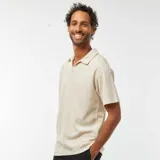Remera tipo polo color beige claro, de manga corta y corte holgado.