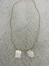 Collar dorado con cadena fina y dos dijes rectangulares de nácar con grabados religiosos.
