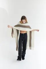 Ruana artesanal color beige con rayas horizontales rojas y amarillas, y flecos en el borde inferior.