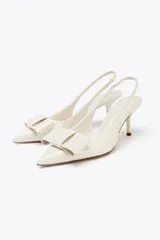 Zapato de tacón destalonado color blanco acharolado, con punta fina, lazo decorativo y tira trasera elástica.