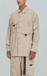 Camisa beige de manga larga, estilo técnico con múltiples bolsillos delanteros y un bolsillo en la parte inferior de la espalda, botones en la cartera y mangas, calce oversize, confeccionada en textil ligero suave al tacto.