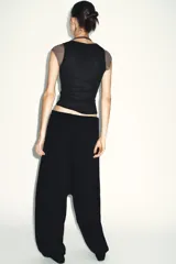 Top de manga caída, con efecto de doble capa. La capa exterior es negra y ajustada, mientras que la capa interior, visible en mangas y cuello, es de color marrón topo.