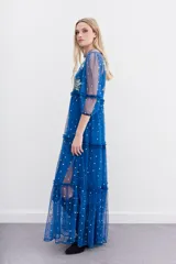 Vestido largo de tul bordado color azul con hilo de lurex y lentejuelas plateadas. Tiene escote en V cruzado, mangas 3/4 con volados y puños elásticos, frunces en la cintura y viso a tono.